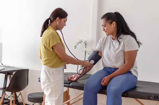 Young woman of Pacific Islander descent at risk of developing diabetes having blood pressure measured by doctor at routine medical appointment.