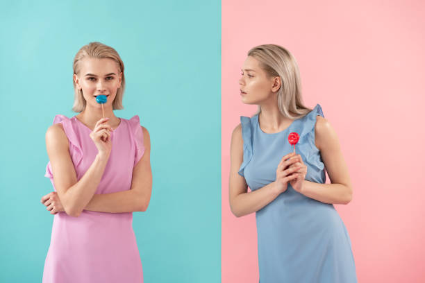 Woman having fancy for friends candy Two girls holding sweets on stick. One looking at another with envy. Isolated on blue and pink background envy stock pictures, royalty-free photos & images
