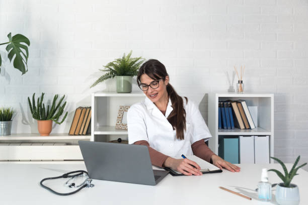 Woman health care medic worker with stethoscope looking at laptop web camera, doctor make video call interact through internet talk with patient provide help online counseling and therapy concept stock photo