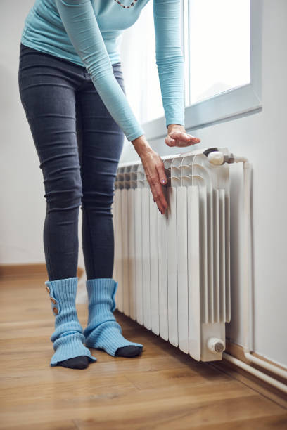 Woman heating her hands on the radiator during cold winter days. stock photo