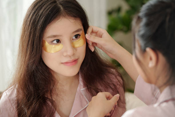 Woman helping friend to apply undereye patches Young woman helping friend to apply undereye patches to get rid of dark circles and wrinkles dark circles stock pictures, royalty-free photos & images