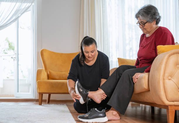 Woman helping her elderly mother in wearing shoes at home stock photo