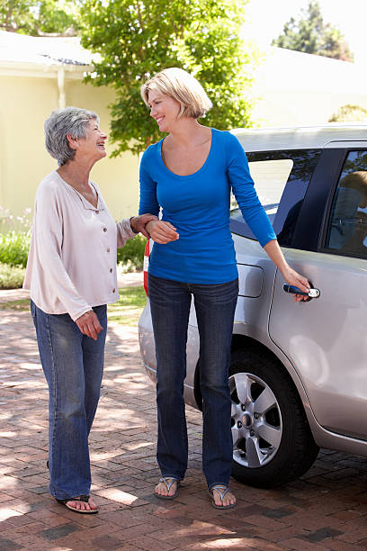 woman helping senior lady into car - house with 2 cars bildbanksfoton och bilder