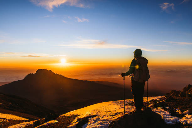Woman hiker achieved the dream enjoying the awe sunrise from the top of Kilimanjaro mountain Woman with backpack and hiking poles got to the top of Africa - Mount Kilimanjaro and looking at the beautiful bright sunny sunrise above the Meru mountain mt kilimanjaro photos stock pictures, royalty-free photos & images
