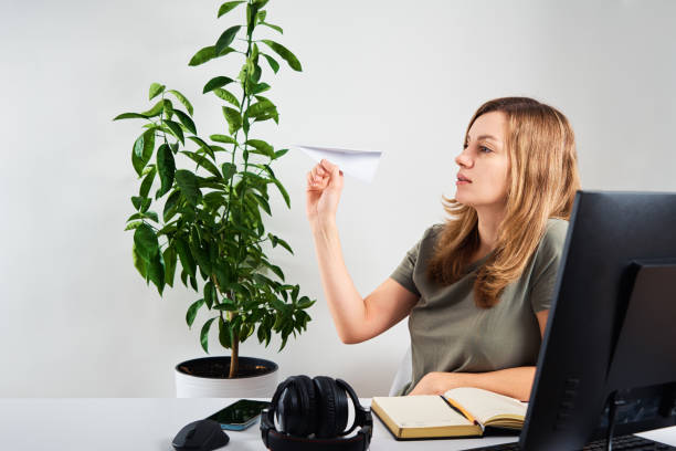 Woman hold paper plane while working at home office Woman launches paper plane and dreaming about vacation while sitting at computer at remote work wasting time stock pictures, royalty-free photos & images