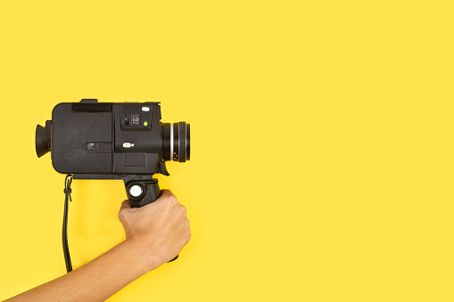 Woman holding an eight mimlimiters camera on a yellow background with copy space