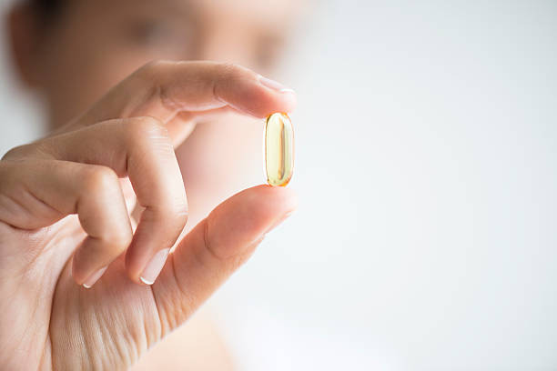 Woman Holding And Showing Omega 3 Capsule Woman holding omega 3 capsule. fish oil stock pictures, royalty-free photos & images