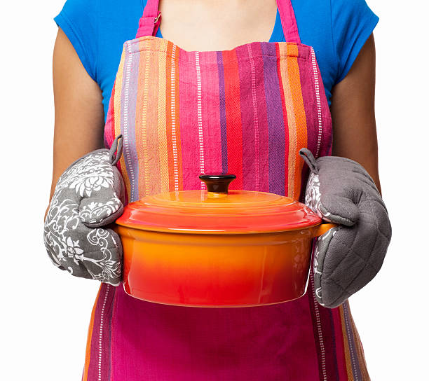 Woman Holding Casserole Dish - Isolated Midsection of woman in a multi colored apron holding a casserole. Square. Isolated on white. casserole dish stock pictures, royalty-free photos & images
