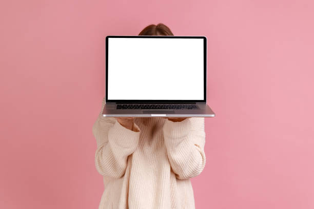 Woman holding laptop in hands, hiding her face behind notebook with empty display with copy space. stock photo