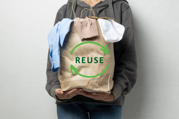 Woman holding paper bag with Reuse sign and full of apparel.Pack with reuse symbol.Clothes for donation or recycling Woman holding paper bag full of clothes against white empty wall.Concept of reuse,donation stock apparel.Free space slow fashion stock pictures, royalty-free photos & images