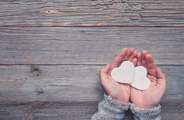Woman holding two white love hearts. A woman is holding them in her hands. There is a rustic wood table underneath her hands. Valentines day or anniversary concept. Copy space.