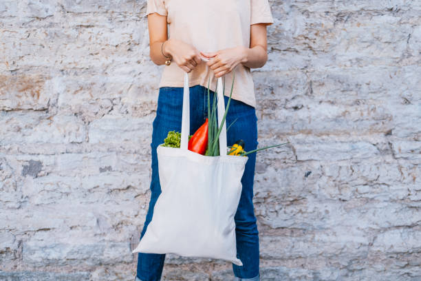 Woman holding white canvas tote bag with vegetables near brick wall. Woman holding white canvas tote bag with vegetables near brick wall. Reusable eco concept. climate action stock pictures, royalty-free photos & images