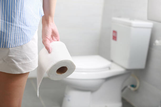 Woman holds toilet paper roll in front of toilet bowl. stock photo