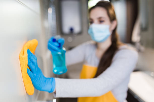 Woman housekeeper wipes the door with rag and using spray disinfectant. Close up of woman with protective mask cleaning bathroom door. Housekeeping concept. CLEANING company stock pictures, royalty-free photos & images