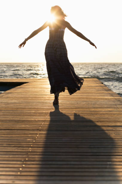 A woman in a dress on a dock with her arms spread stock photo