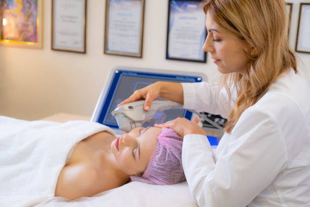 Woman in a spa salon on cosmetic procedures for facial care. Cosmetologist making a woman a therapeutic laser processing on a face. Beautician makes laser procedures on a female face. stock photo