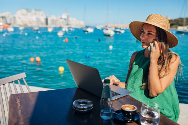 A woman in a summer dress sits at a coffee table by the sea and talks on her mobile phone stock photo