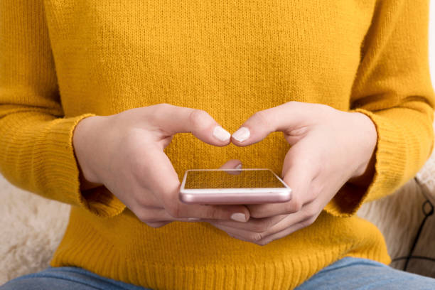 Woman in a yellow pullover- using smartphone stock photo
