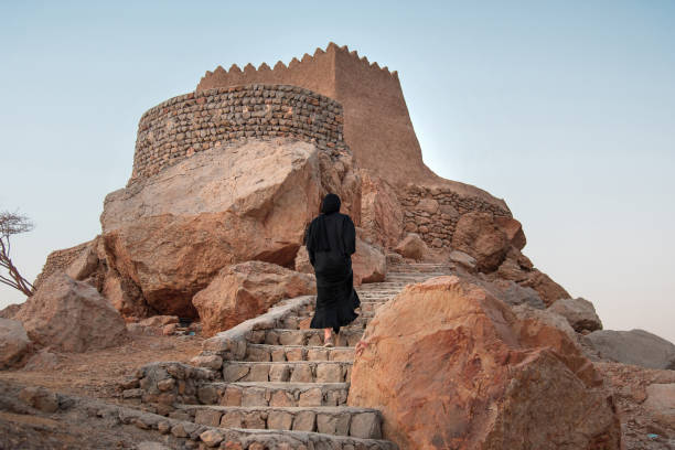 Woman in abaya visiting middle eastern Dhayah Fort in north Ras Al Khaimah, UAE in the desert at sunset Woman in hijab visiting middle eastern Dhayah Fort in north Ras Al Khaimah, United Arab Emirates in the desert at sunset abaya clothing stock pictures, royalty-free photos & images