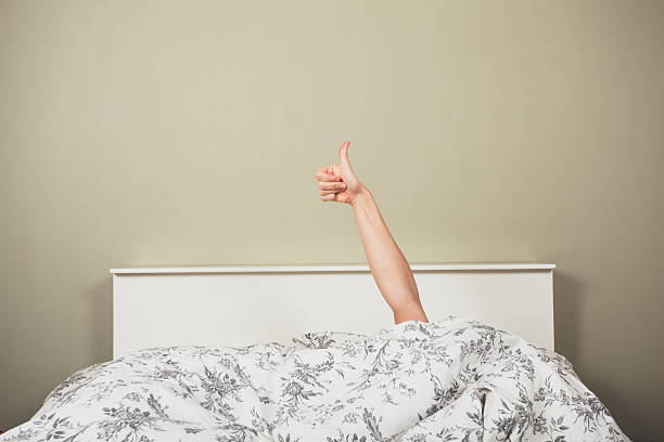 Woman in bed giving thumbs up stock photo