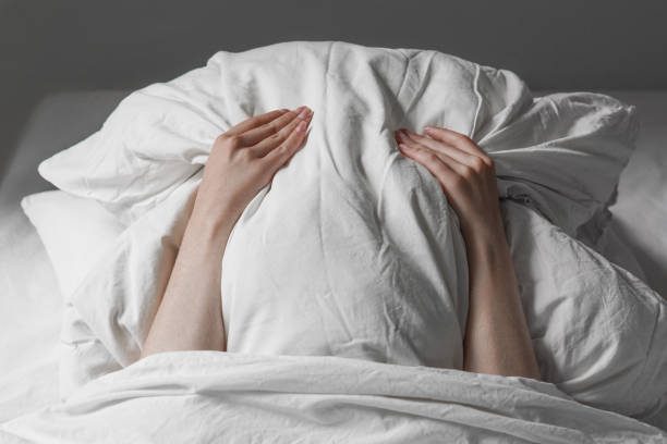 mujer en la cama escondiendo la cara debajo de la almohada - fundas para la cama fotografías e imágenes de stock