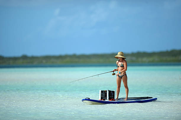 Woman in bikini fishing and paddle boarding stock photo