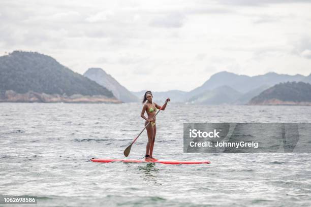 Woman in bikini standing on paddle board in sea