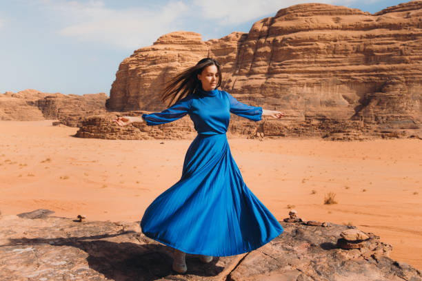 Woman in blue dress contemplating the scenic landscape of Wadi Rum desert Beautiful female in dress walking at the edge of the cliff enjoying the Martian world with red sands and the mountains in Jordan hot middle eastern women stock pictures, royalty-free photos & images