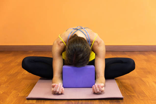 donna in farfalla yin yoga asana con fronte appoggiata su puntello viola - baddha konasana foto e immagini stock