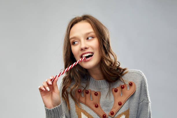 woman in christmas sweater eating candy cane christmas, people and holidays concept - happy young woman wearing ugly sweater with reindeer pattern eating candy cane ugly girl stock pictures, royalty-free photos & images