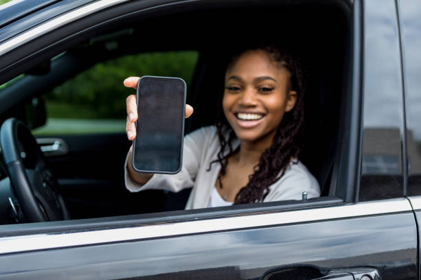 Woman in driver's seat shows phone screen to verify order The young adult woman in the driver's seat shows her phone screen to verify the curbside pickup order. curbsidepickup stock pictures, royalty-free photos & images