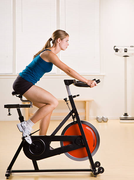 Woman in gym clothes focused on riding a stationary bicycle stock photo