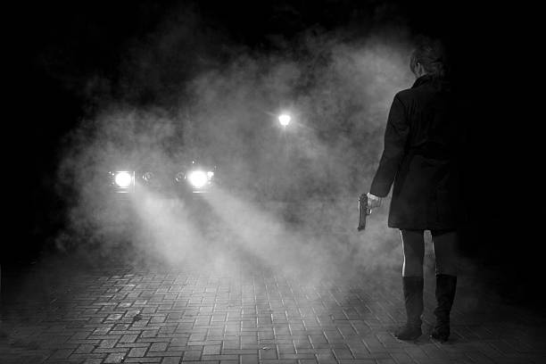 Woman in headlights Awoman holding a gun stands in the headlights of a car Smoking Kills stock pictures, royalty-free photos & images
