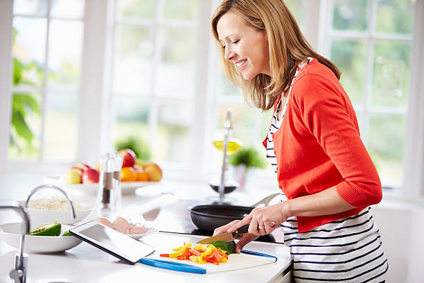 mulher na cozinha seguindo a receita no tablet digital - woman chopping vegetables imagens e fotografias de stock
