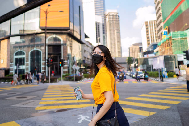 Woman in large city, wearing protective facemask Asian woman with face mask crossing street in bukit bintang shopping district of kuala lumpur bukit bintang stock pictures, royalty-free photos & images