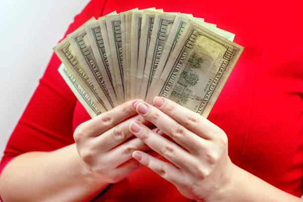 Woman in red dress holding and counting cash money (american dollars) in her hands. Profit and reward, bribe and graft, wealth and lottery win concept stock photo