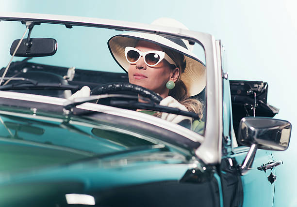 Woman in retro 1960s fashion with hat driving convertible. stock photo