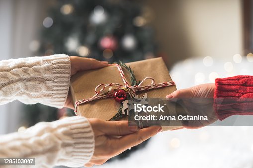istock Woman in sweater giving a wrapped Christmas gift box to child. Glowing snow bokeh, fir tree. Winter holidays 1285103047