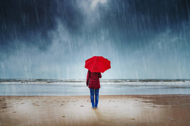 Woman in the rain Lonely woman with red umbrella is standing in the rain watching the sea depression land feature stock pictures, royalty-free photos & images