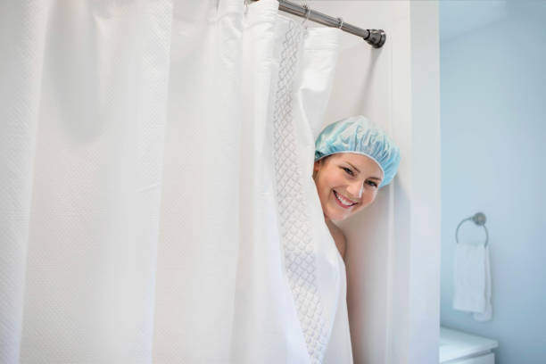 Woman in the Shower A woman smiles as she peeks out of a shower stall wearing a shower cap. shower curtain cleaning stock pictures, royalty-free photos & images