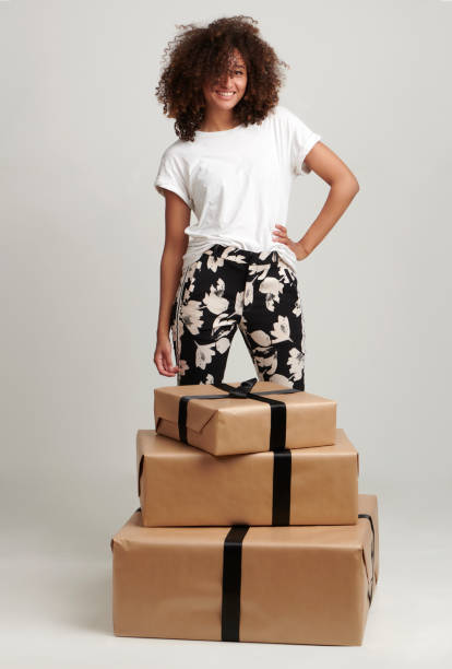 Woman in white shirt standing over three gifts Mixed race woman standing over three gifts in a white shirt and pants. Copy space, space left for own text. happy birthday in danish stock pictures, royalty-free photos & images