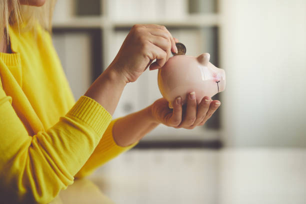 woman inserts a coin into a piggy bank - investment imagens e fotografias de stock