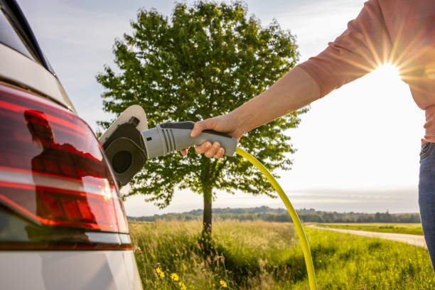 woman inserts a power cord into an electric car for charging on green landscape - electric car woman bildbanksfoton och bilder
