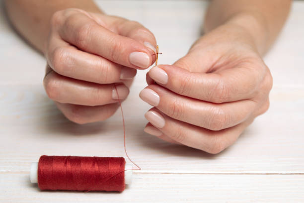 A woman inserts a red thread into a needle. stock photo