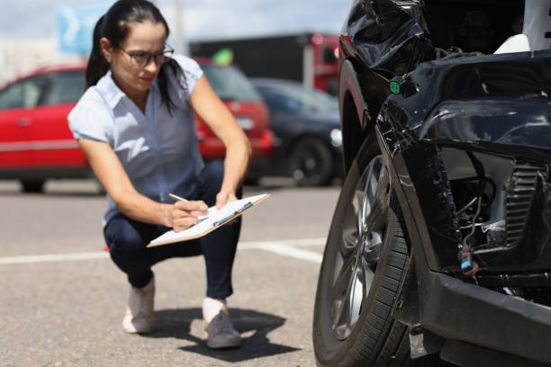 Woman inspector writing in documents on clipboard near broken car. Auto insurance concept stock photo