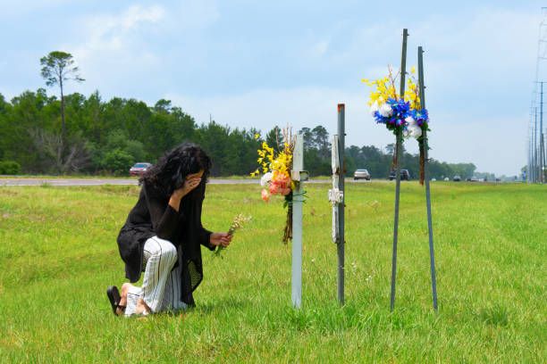 A woman is kneeling down and grieving crosses beside a busy road marking where her friend was killed in a  drunk driving car wreck stock photo
