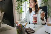 チア/シリアルプリンを食べながらホームオフィスからコンピューターで作業する日本人女性