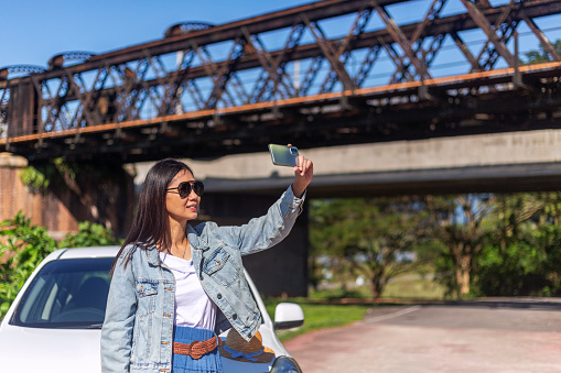 solo female tourist taking selfie on road trip, stop by the side of scenery historical railroad bridge