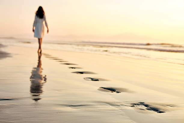 Woman leaving footprints while walking on wet sand at sunset stock photo