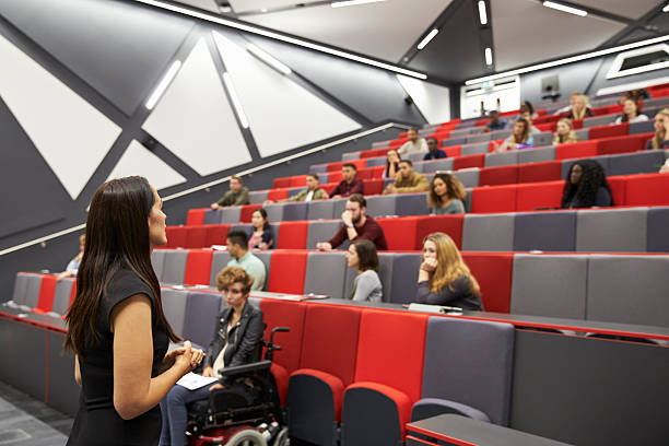 Woman lecturing students in a university lecture theatre Woman lecturing students in a university lecture theatre universities in uk stock pictures, royalty-free photos & images